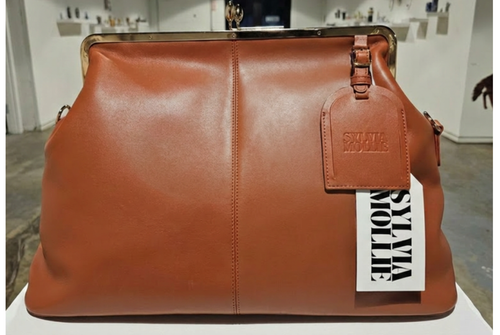The Fannie Bag in cognac leather with a gold-tone kiss-lock frame and embossed hangtag