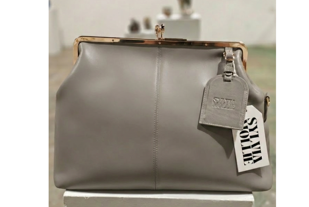 The Fannie Bag in grey leather with a gold-tone kiss-lock frame and embossed hangtag