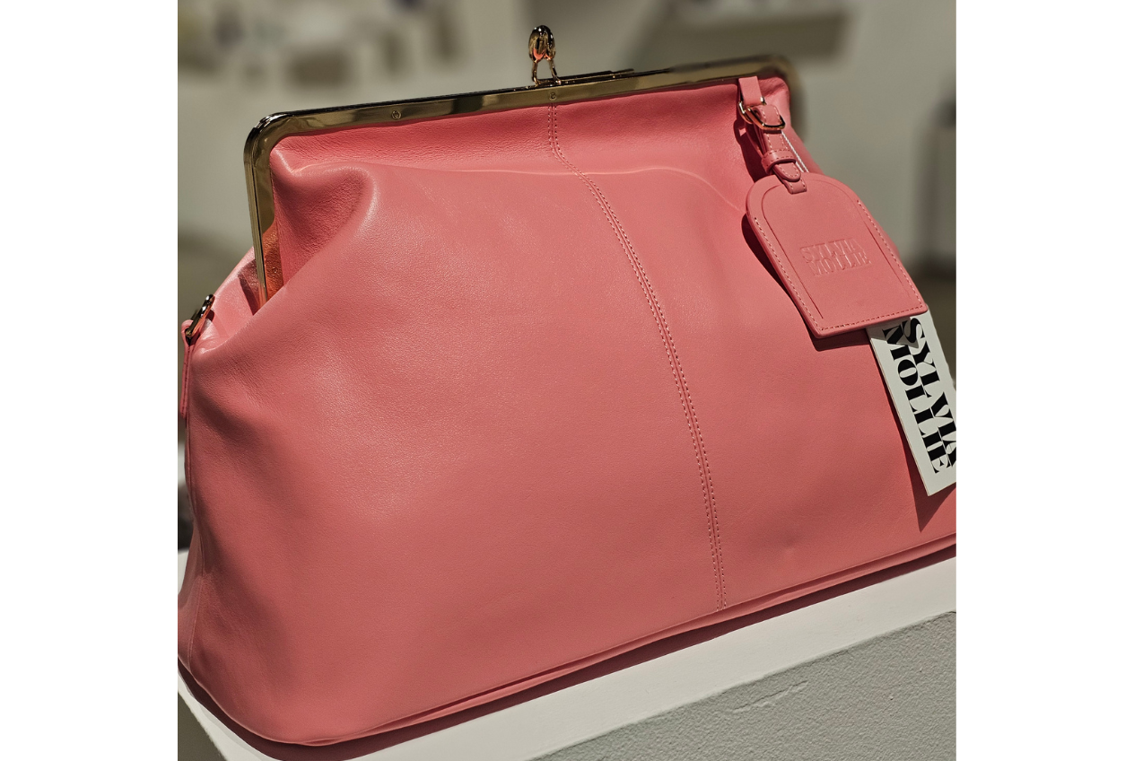 Coral pink kiss-lock leather handbag with a matching hangtag