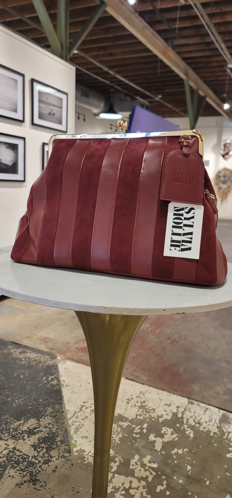 Burgundy striped handbag with a leather hangtag on a white table