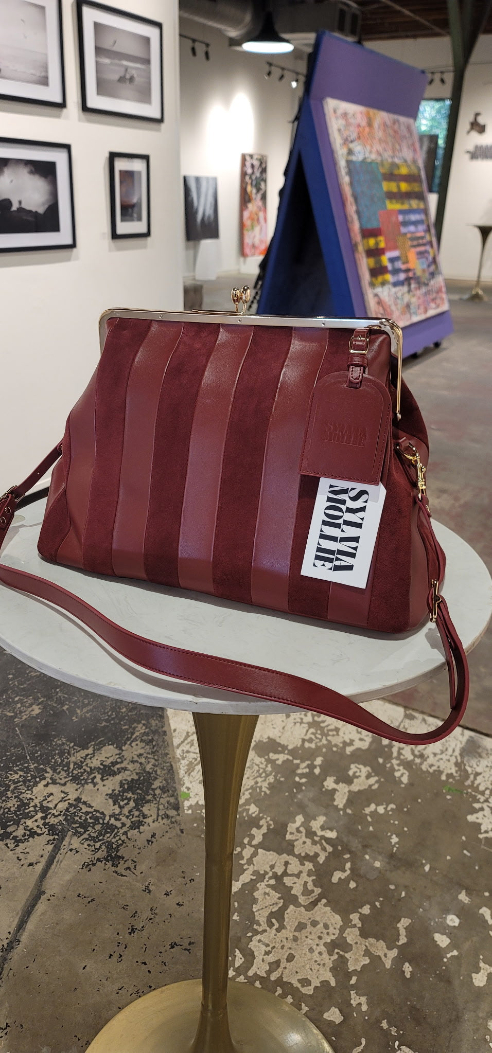 Red striped handbag with a visible brand logo on a white pedestal table.